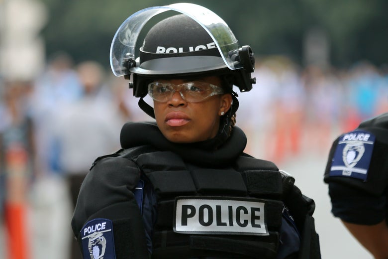 A female police officer wearing a helmet, safety goggles, and a protective vest