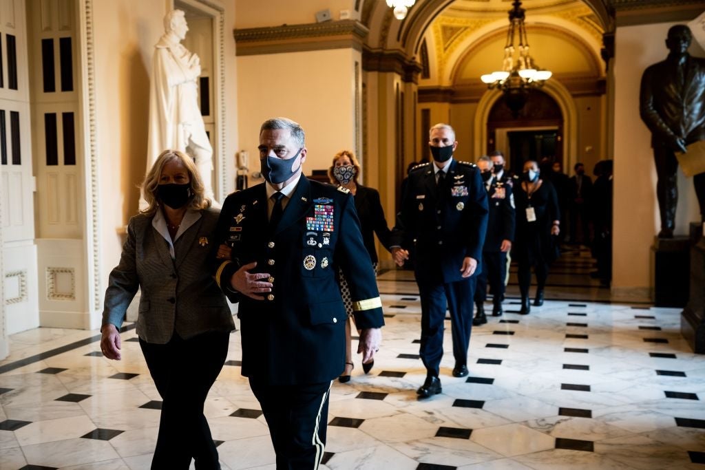 Milley, wearing a uniform and a mask, walks with his wife through a tiled hallway.