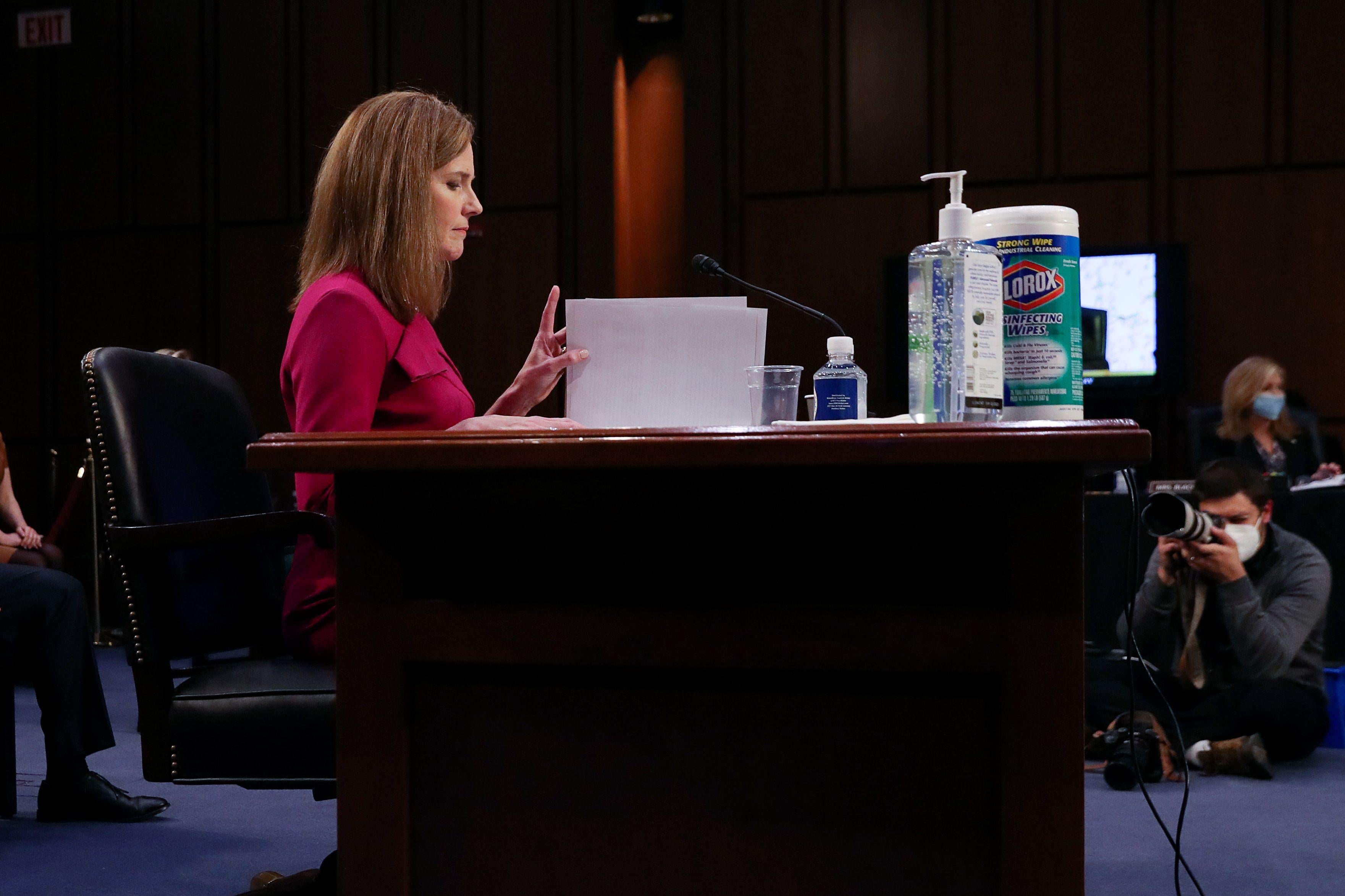 In profile, Amy Coney Barrett sits at a desk and reads a paper.