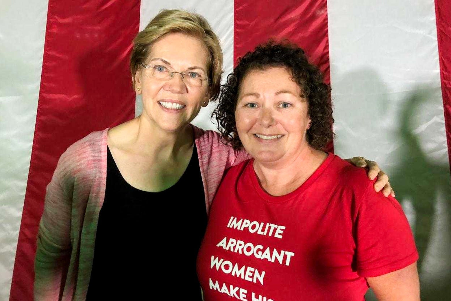 Elizabeth Warren and Mia Pinto pose in front of an American flag.