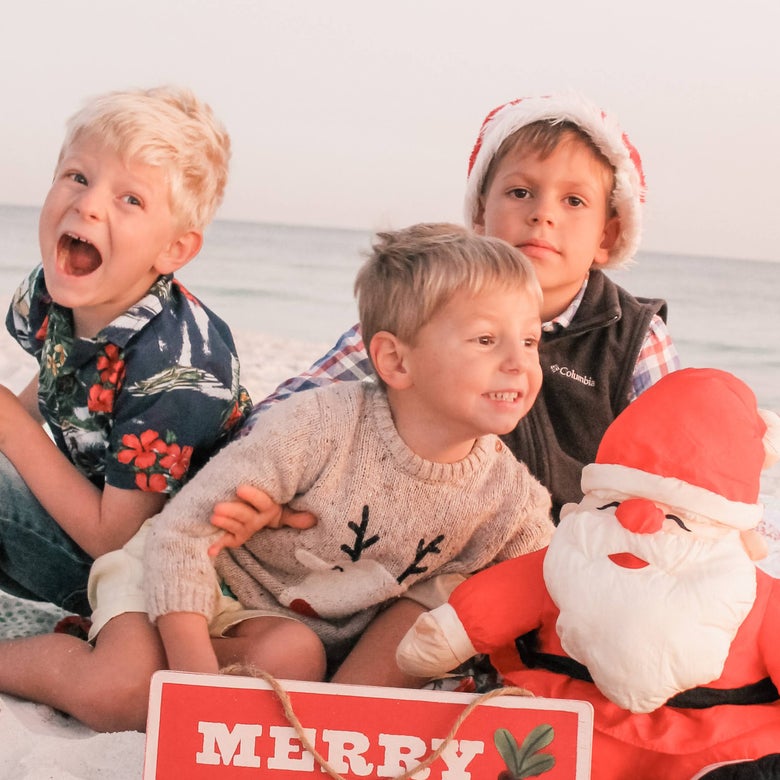 Oliver, Henry, and Teddy sitting on the beach posing with a little Santa and 'Merry Christmas' holiday sign.