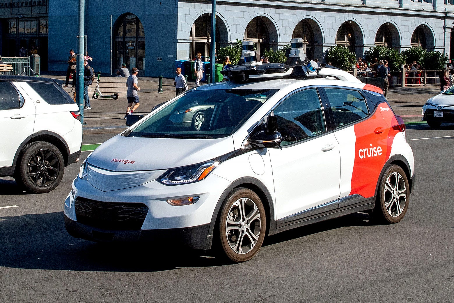 A Cruise taxi, white with a large red stripe, on a test drive. It has a camera-like device on top.