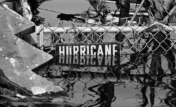 Tangled debris floating around fence with a sign reading HURRICANE in the aftermath of Hurricane Betsy.