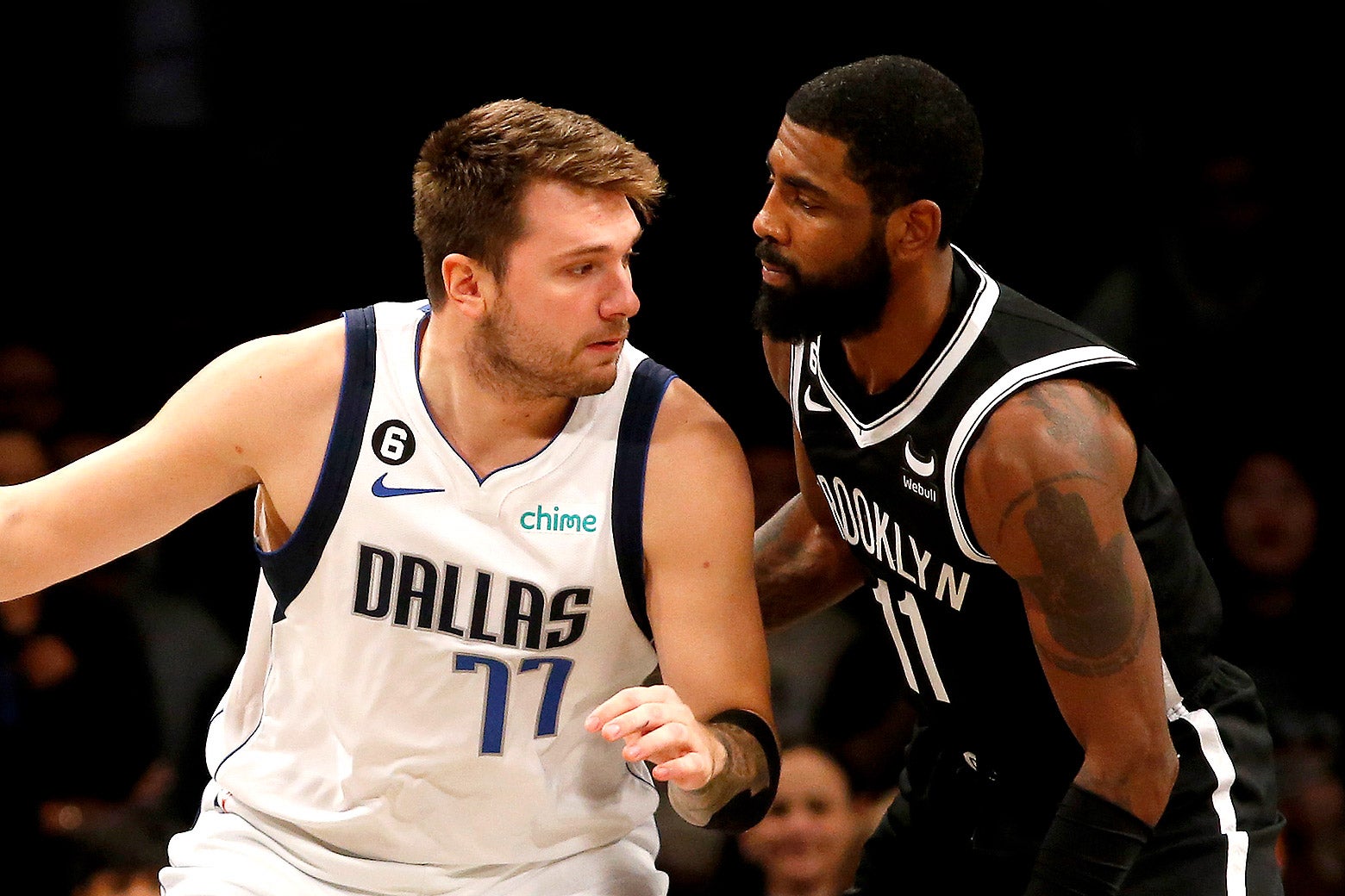 Luka Doncic, in a white Dallas Mavericks jersey, attempts to maneuver around Kyrie Irving, in a black Brooklyn Nets jersey, during a game.