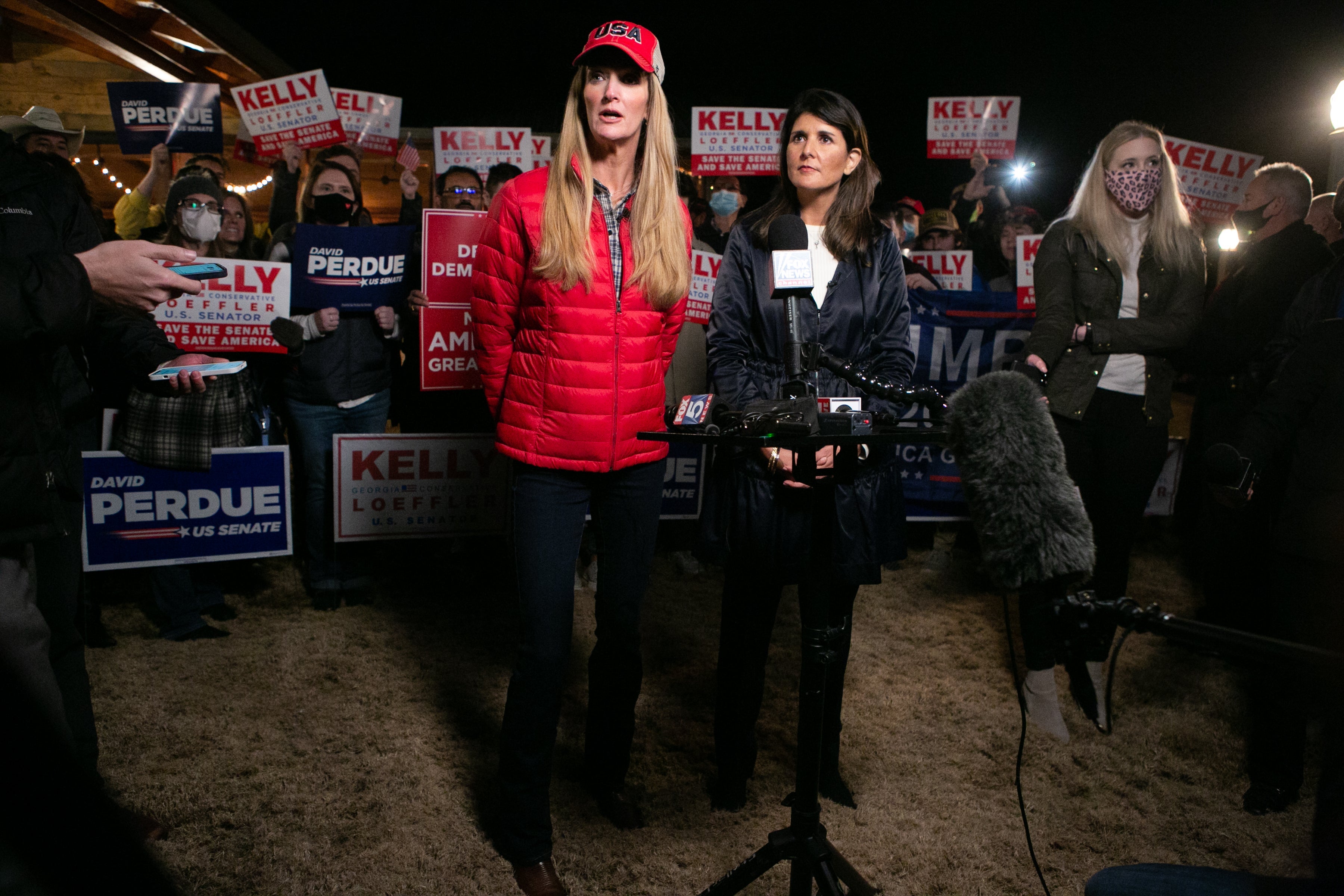 Haley, wearing a blue jacket, watches while Loeffler speaks to reporters in front of a crowd of supporters.