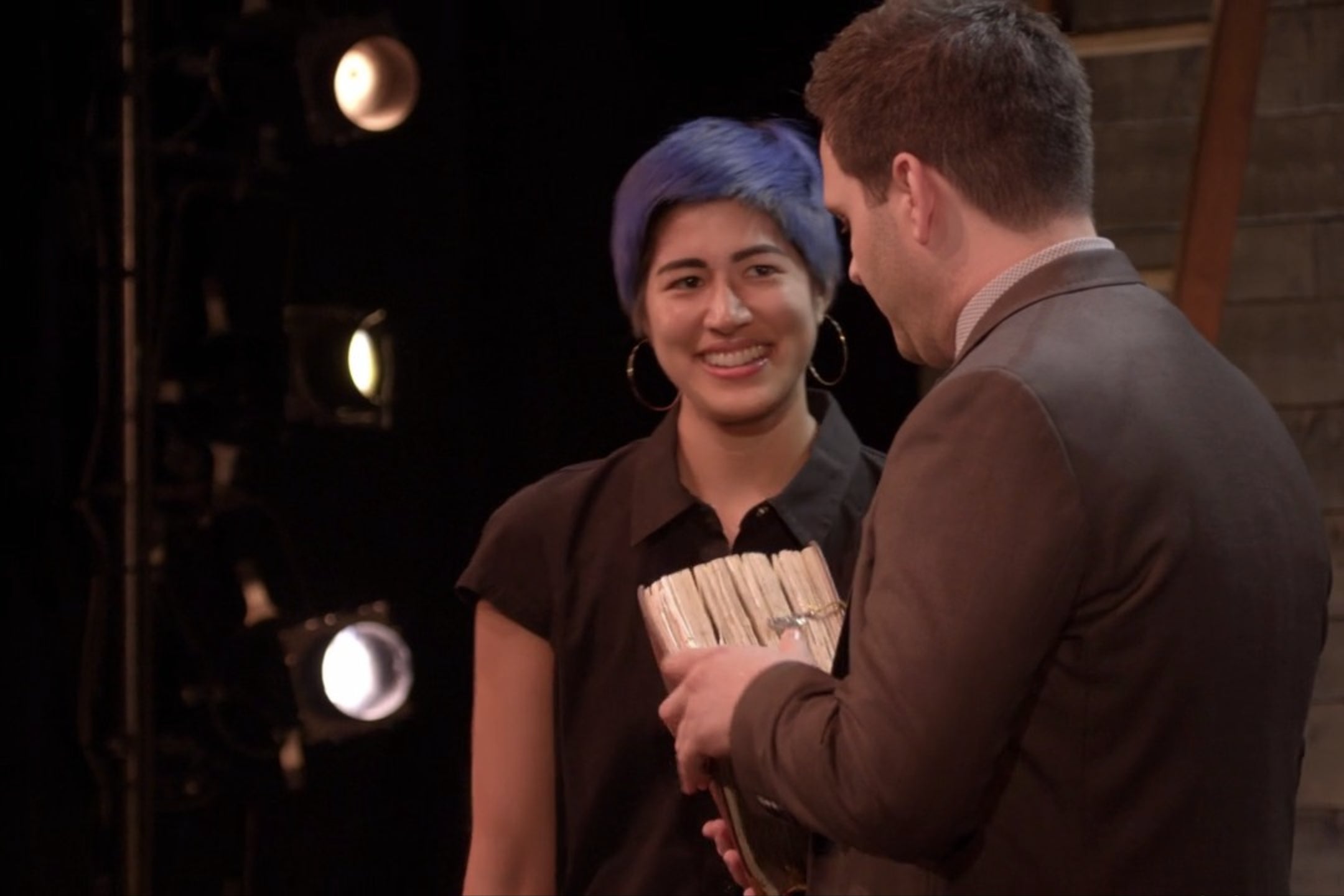 Emma Sulkowicz hands a large book to Derek DelGaudio.