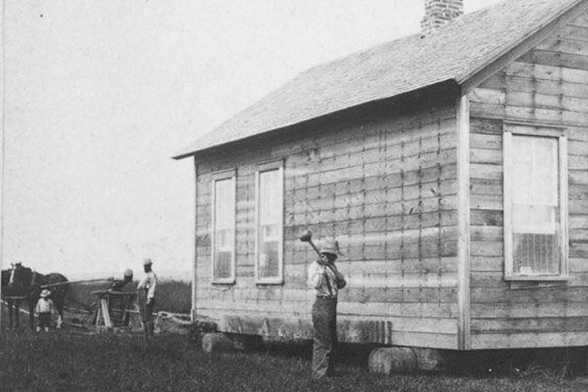 A man stands beside a house on a large cart.