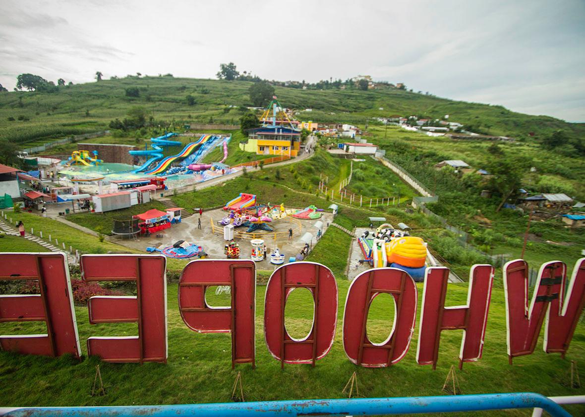 From the gates of Whoopee Land, green rice fields, a Buddhist monastery, mud huts, water slides, and amusement park rides are all visible. 