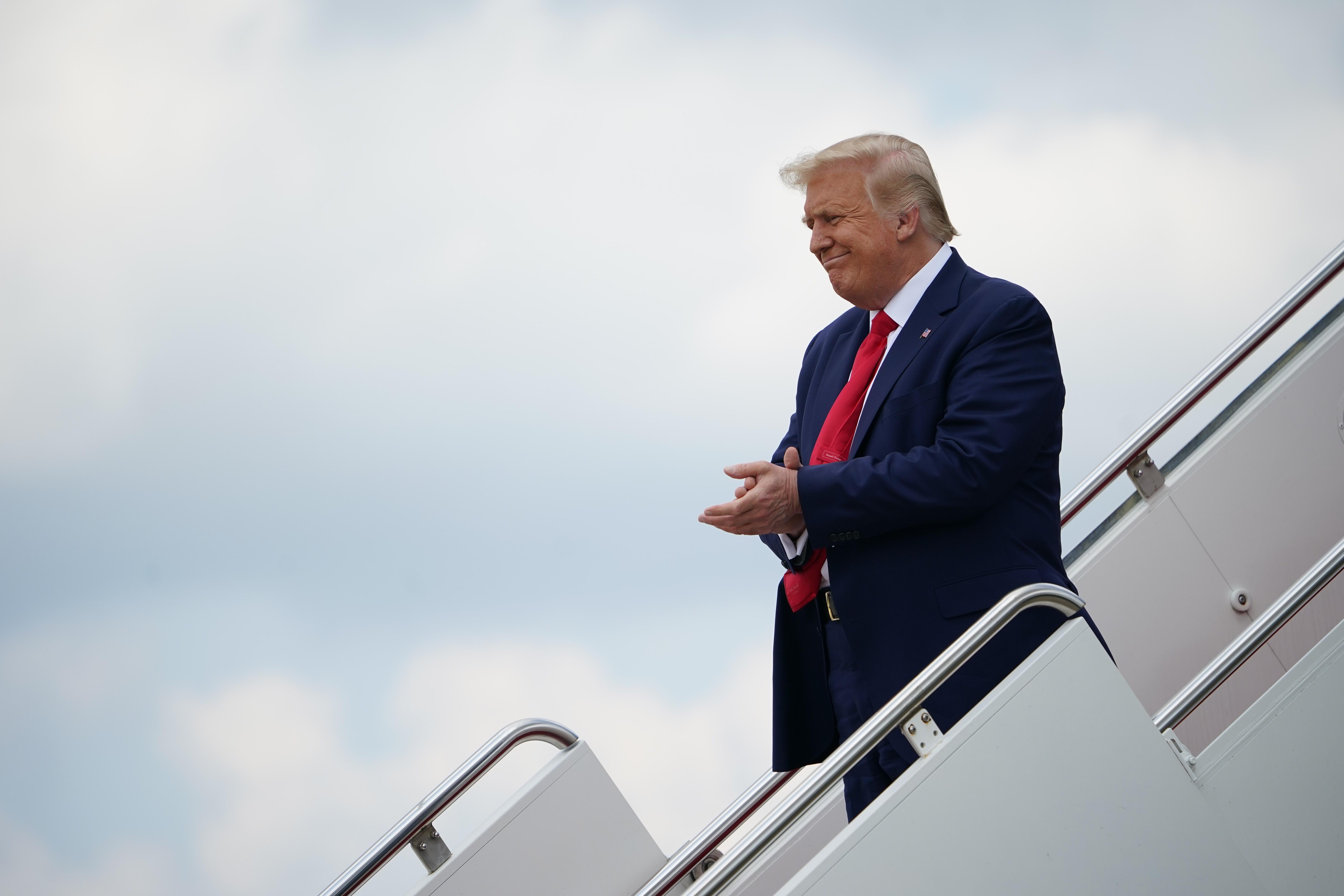 Trump stands on the steps of Air Force One, clapping and smiling.