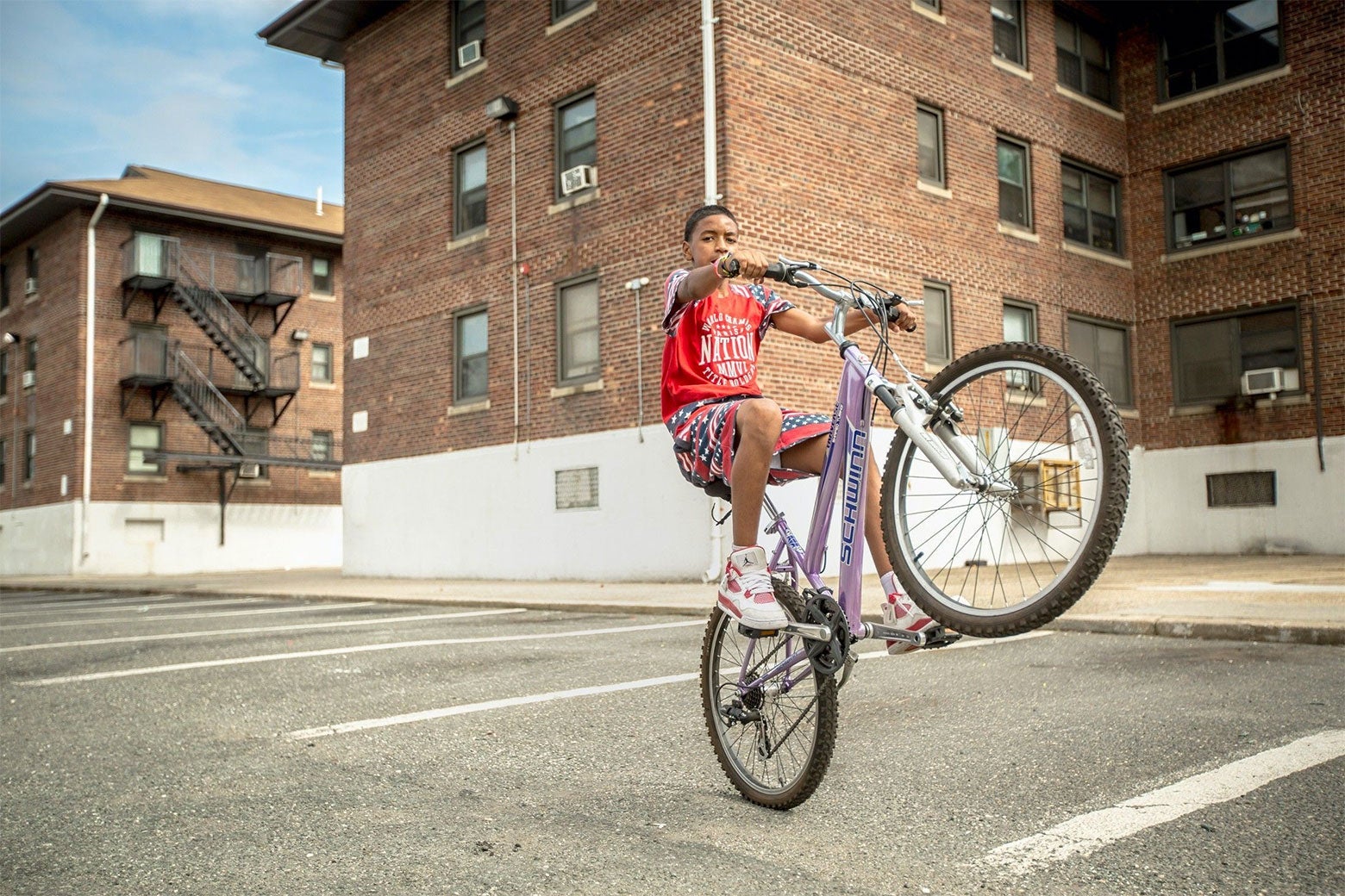 A boy rides his bike on an apartment parking lot.