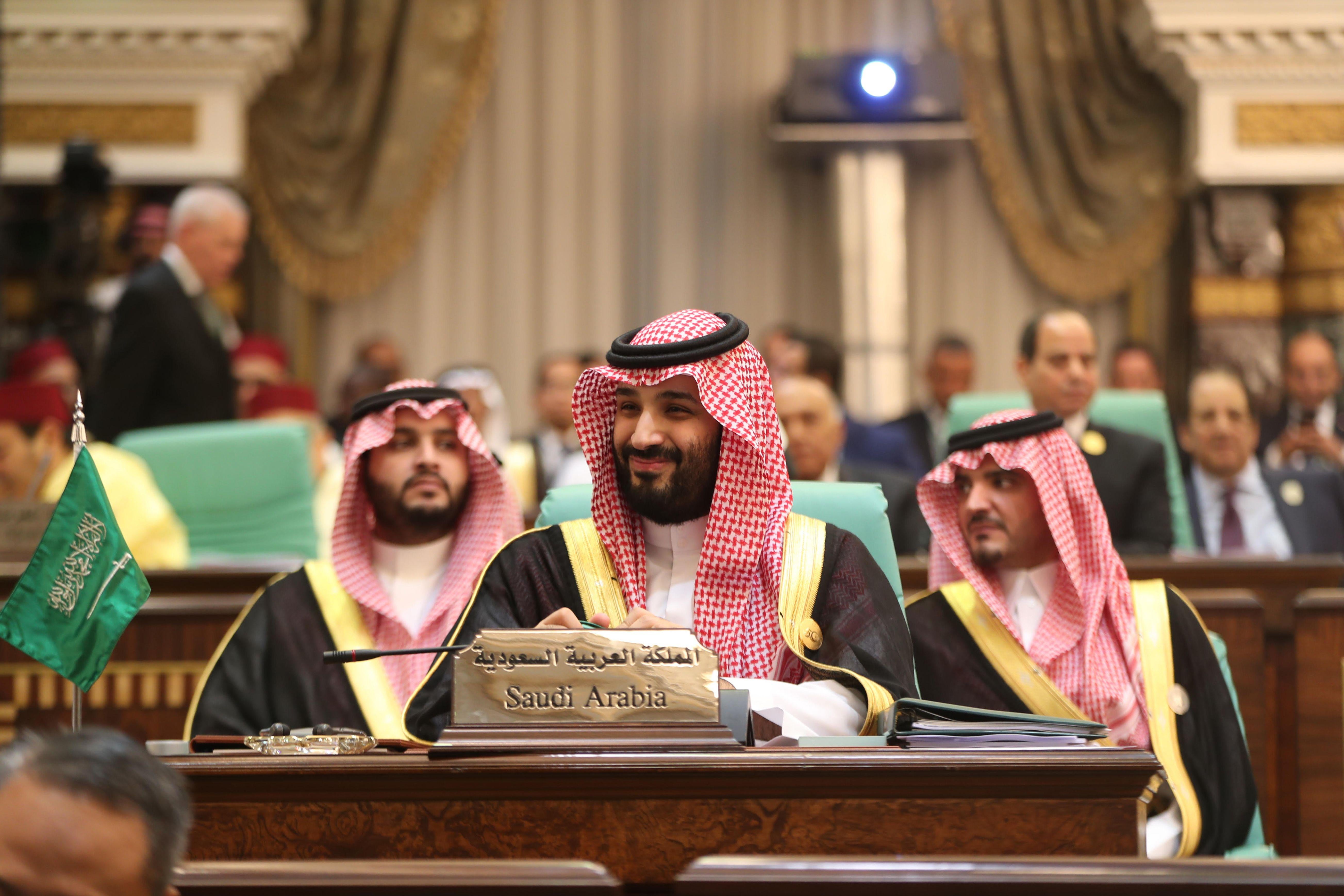 A smiling Mohammed bin Salman sits at a conference table. 