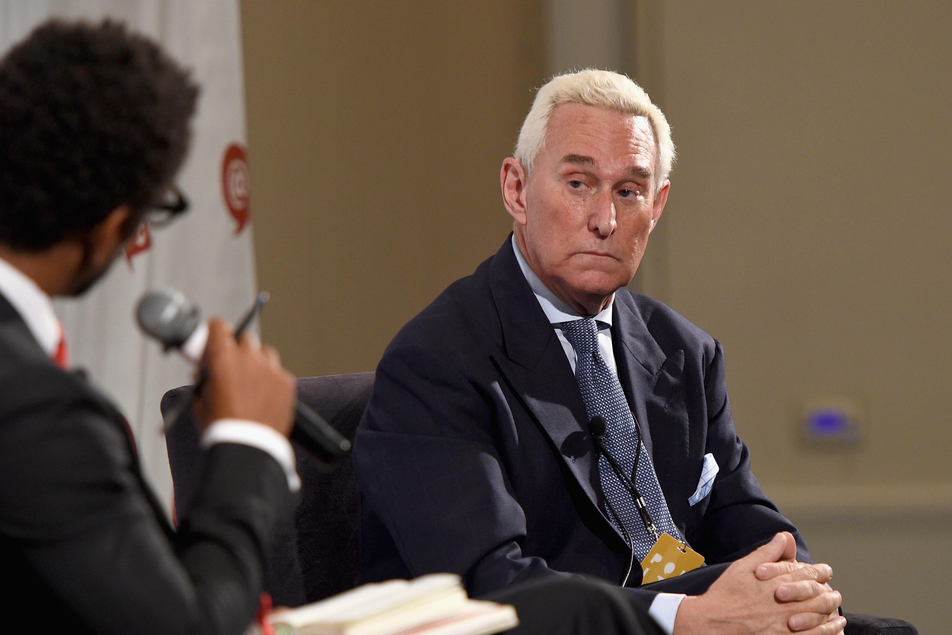 Roger Stone looks warily toward an interviewer holding a microphone.