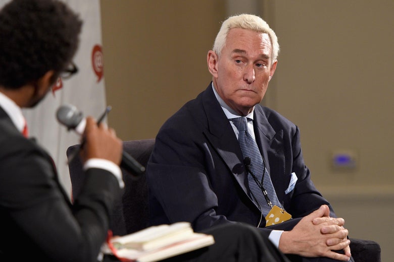 Roger Stone looks warily toward an interviewer holding a microphone.