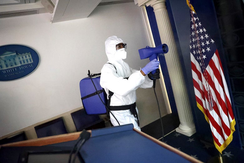 A person in a white full-body protective suit cleans the briefing room.