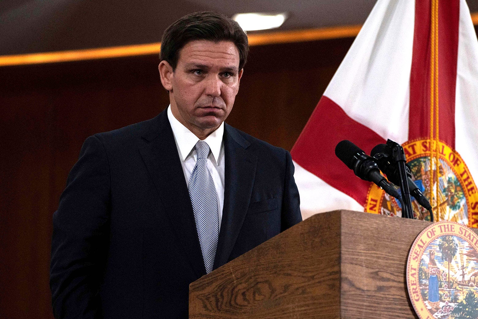 Florida Governor Ron DeSantis standing at a podium with a concerned look on his face, following his "State of the State" address in Florida.