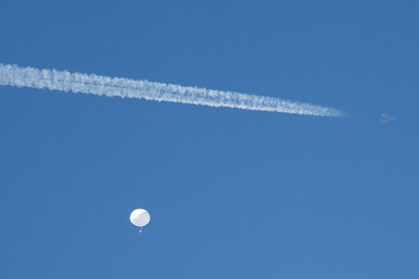 A big balloon in the sky, with a vapor trail from a jet speeding by.