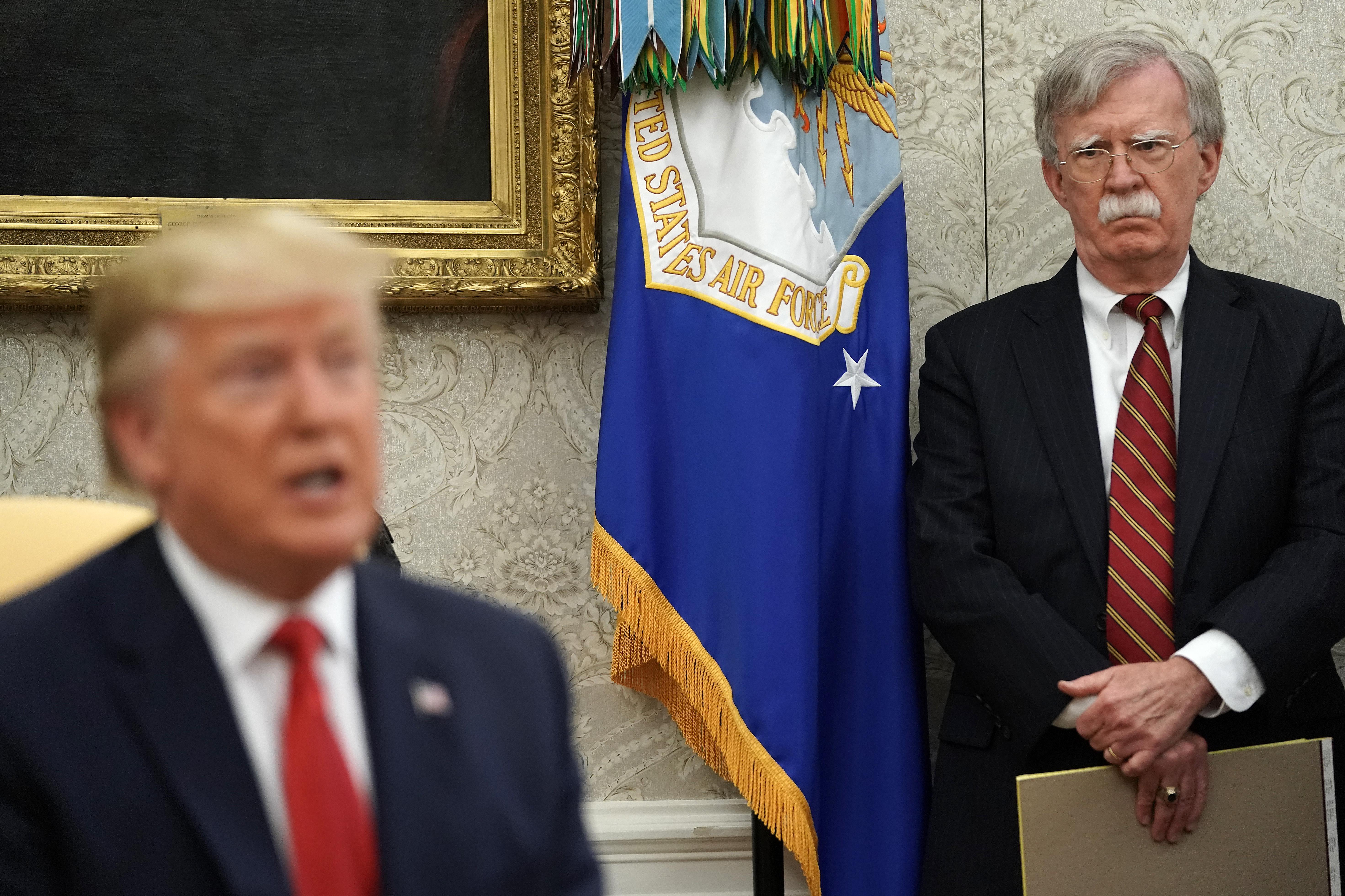 Former White House National Security Advisor John Bolton stands behind President Trump in the Oval Office. 