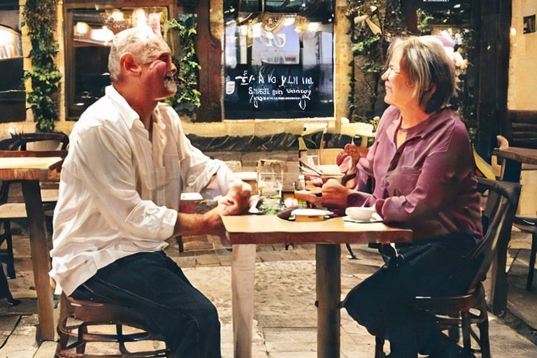 Another couple holding hands and smiling in a restaurant, this time sitting across from each other at a table.