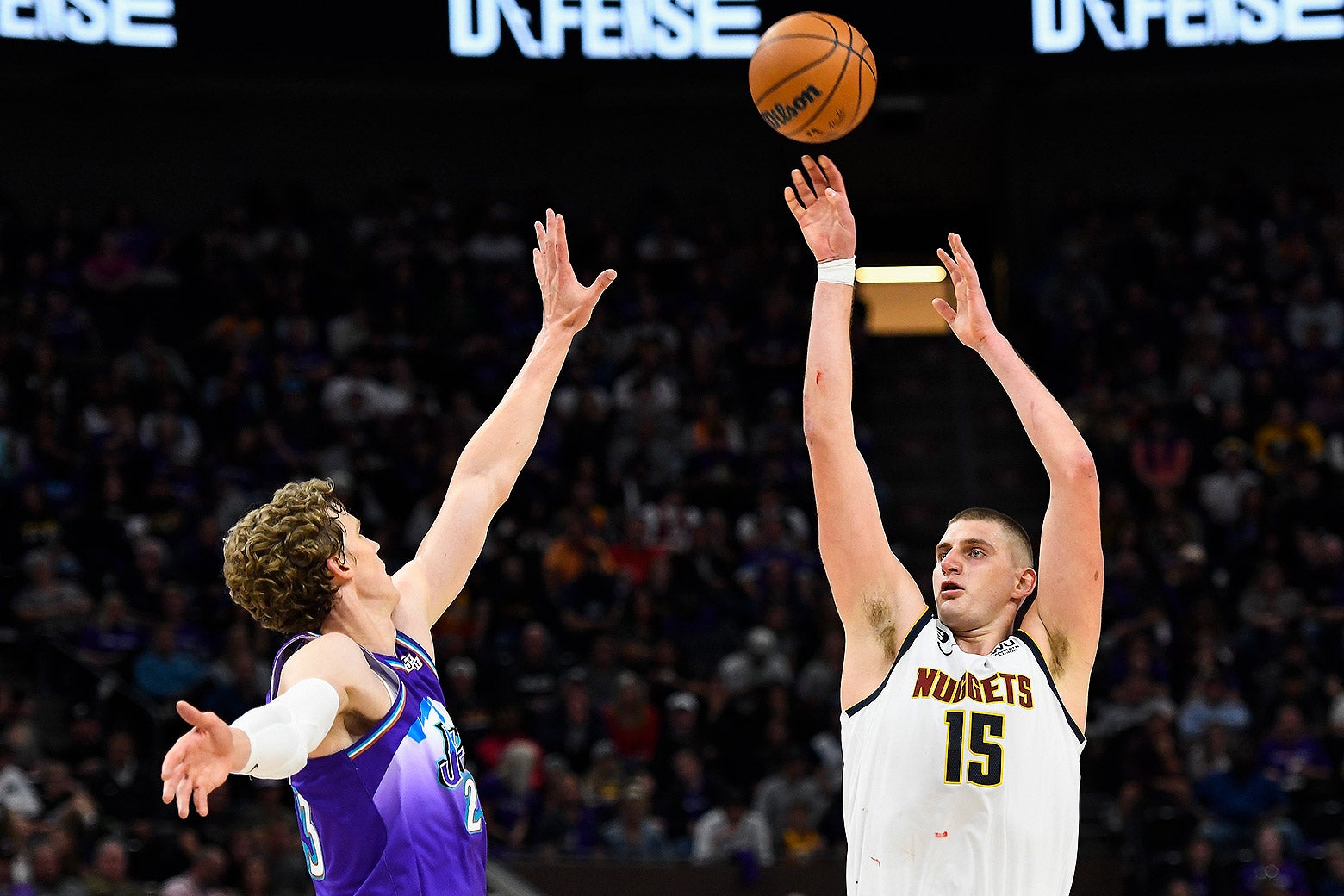 Jokic, wearing a white jersey, shoots a three-pointer.
