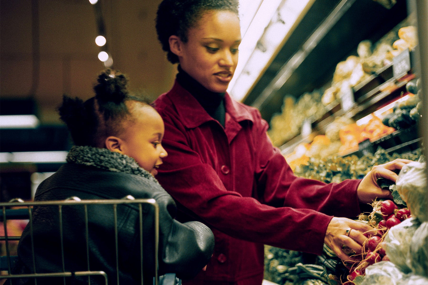 Black woman and child grocery shopping in produce section.