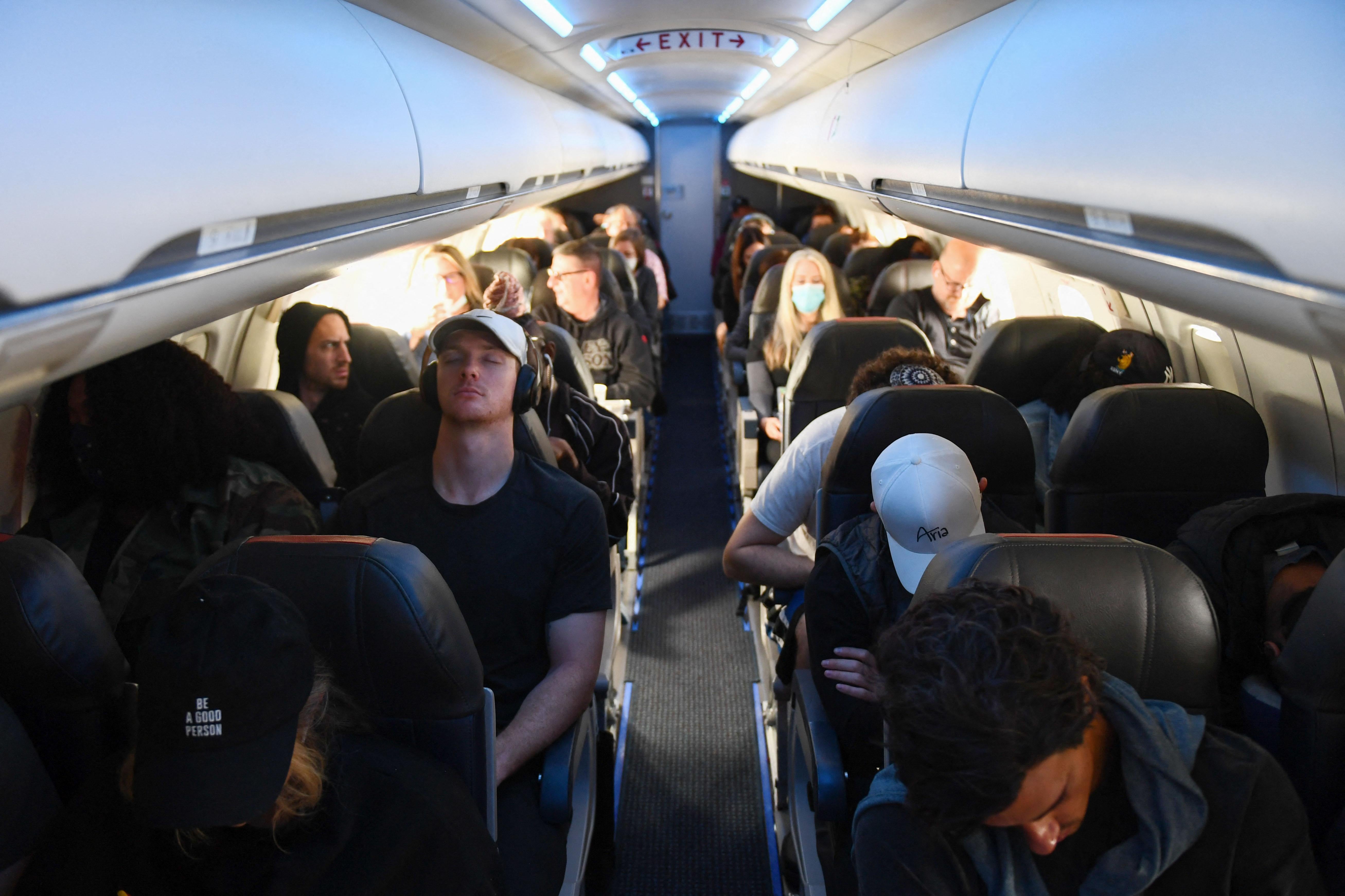 A mix of passengers wearing masks and not wearing masks in the cabin of an airplane.
