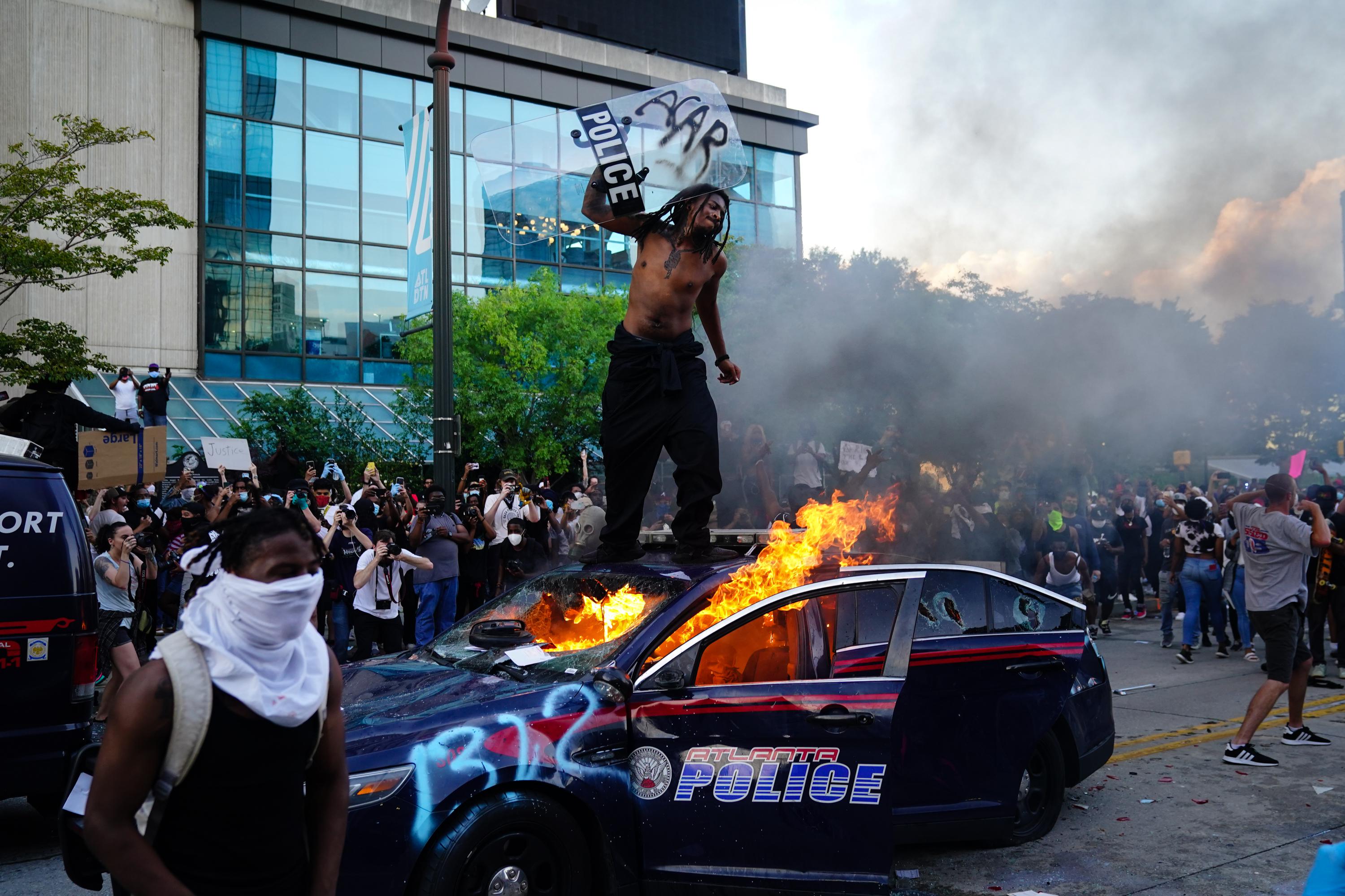 A man stands on top of a burning police car during a protest on May 29, 2020 in Atlanta, Georgia.