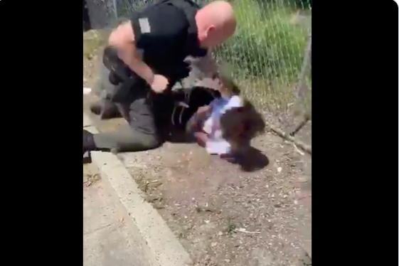 A police officer winds his fist to punch a 14-year-old boy lying on the ground.