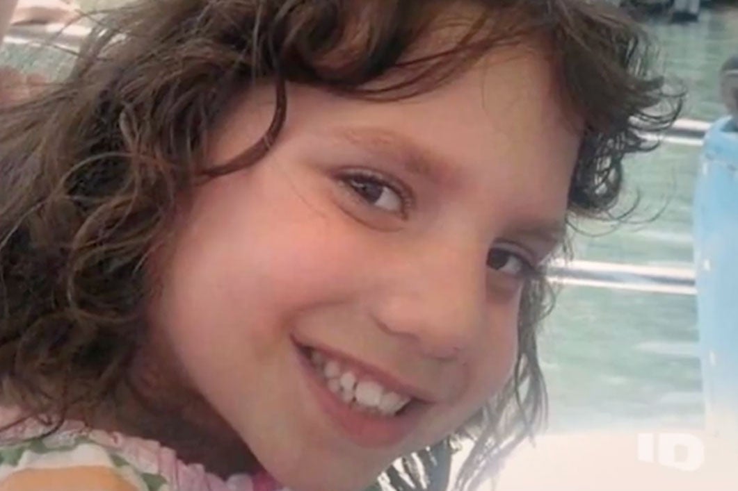 A young girl with curly brown hair smiles in a home video.