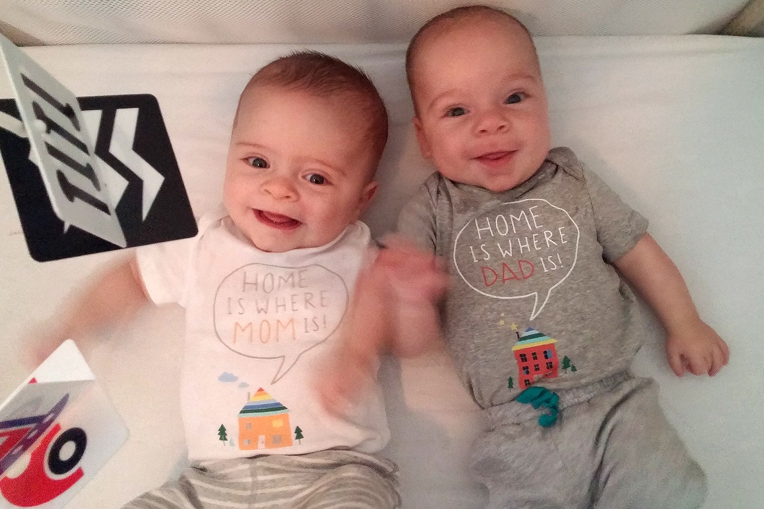 Two infant boys lie in a crib smiling.