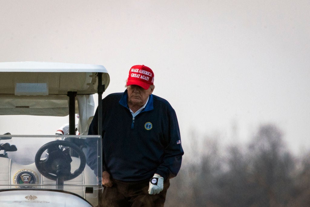Trump, who is wearing a windbreaker and a Make America Great Again hat, climbs into a golf cart.
