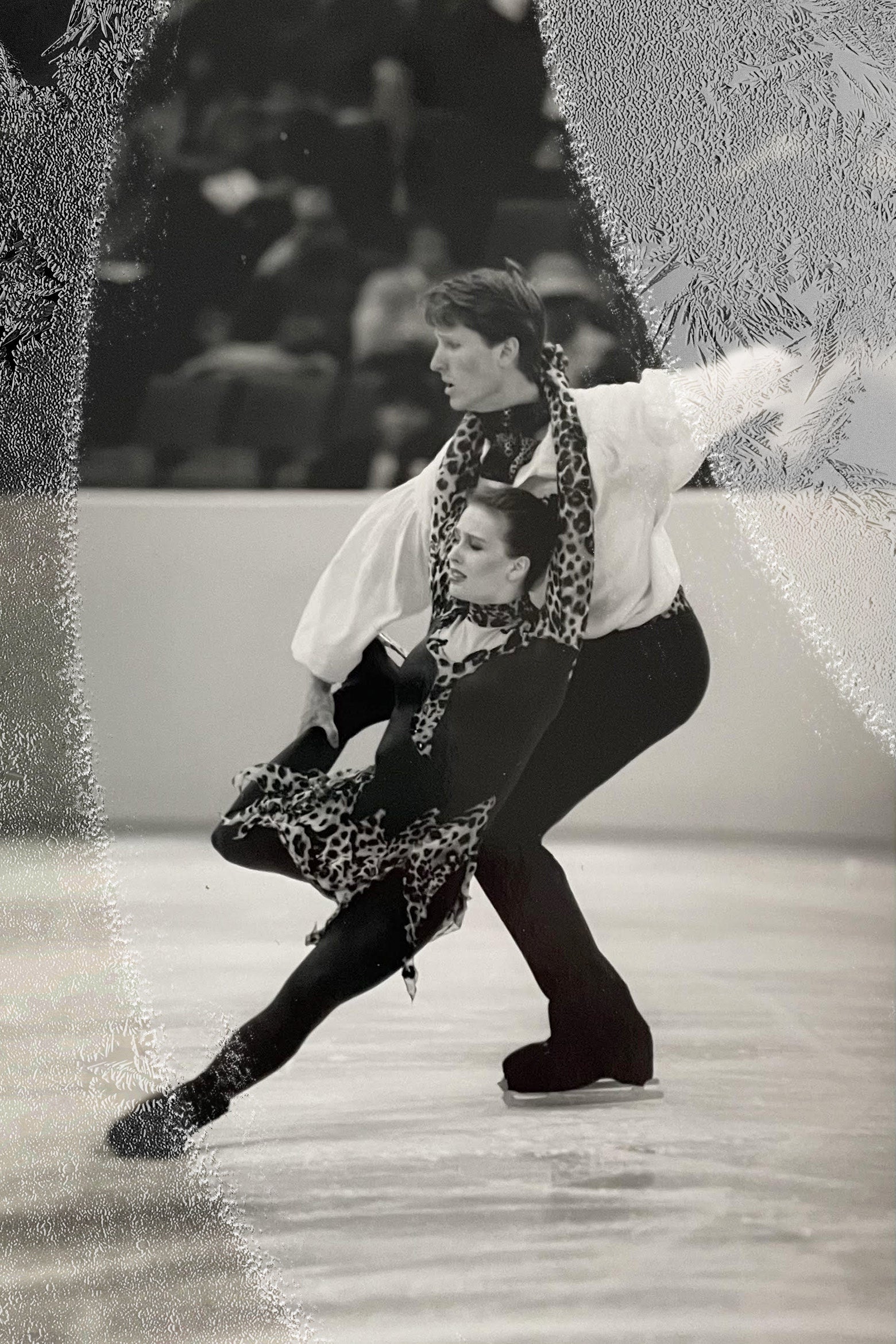 Two ice dancers lean on each other while skating, each balanced on one leg.