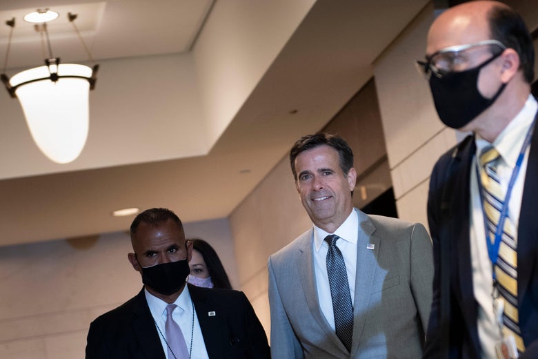 Ratcliffe, maskless and smiling, stands between two men wearing masks in a hallway