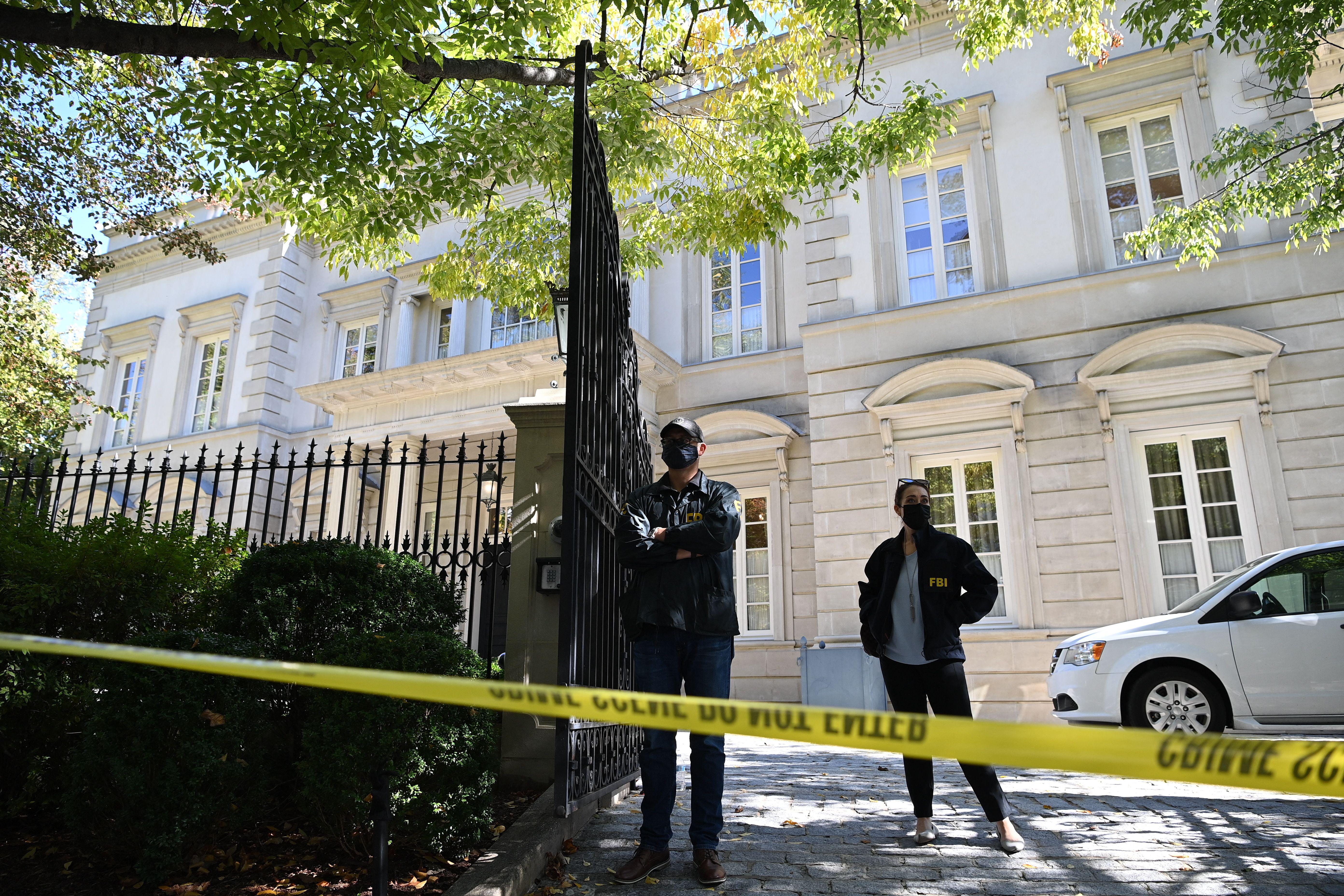 Agents wearing FBI jackets stand guard in front of a mansion closed off with crime scene tape