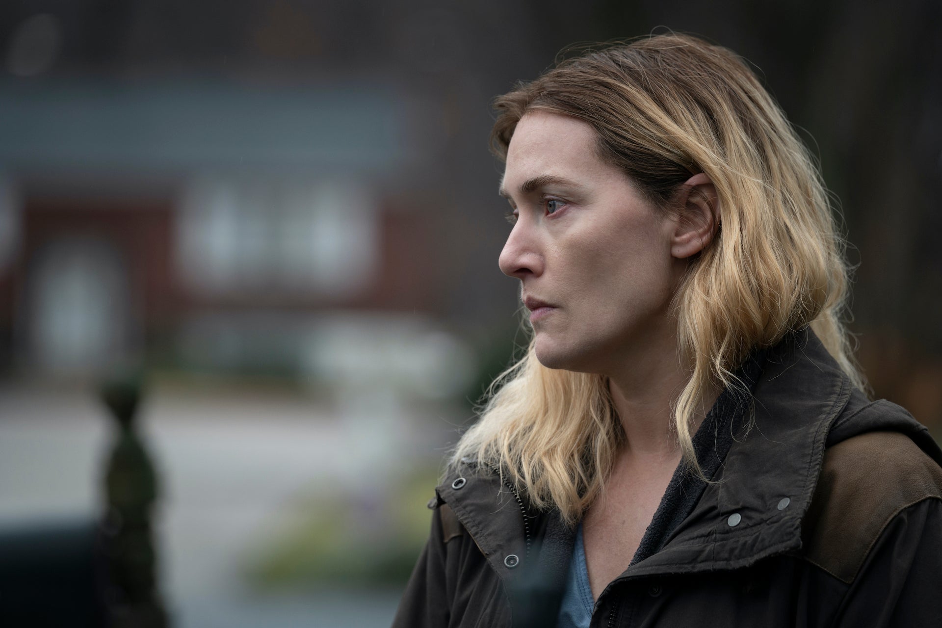 Side profile of Kate Winslet as Mare looking pensive, standing outside in a jacket