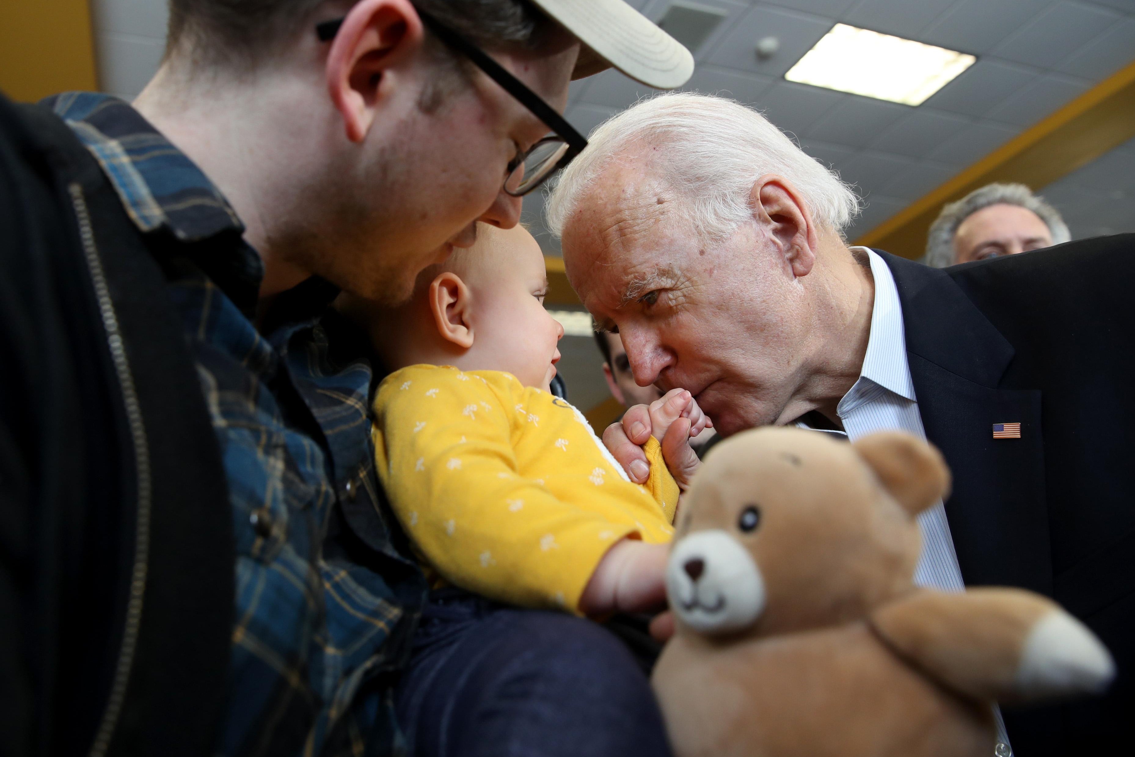 Joe Biden stares into the eyes of a small baby and holds the child's hand.