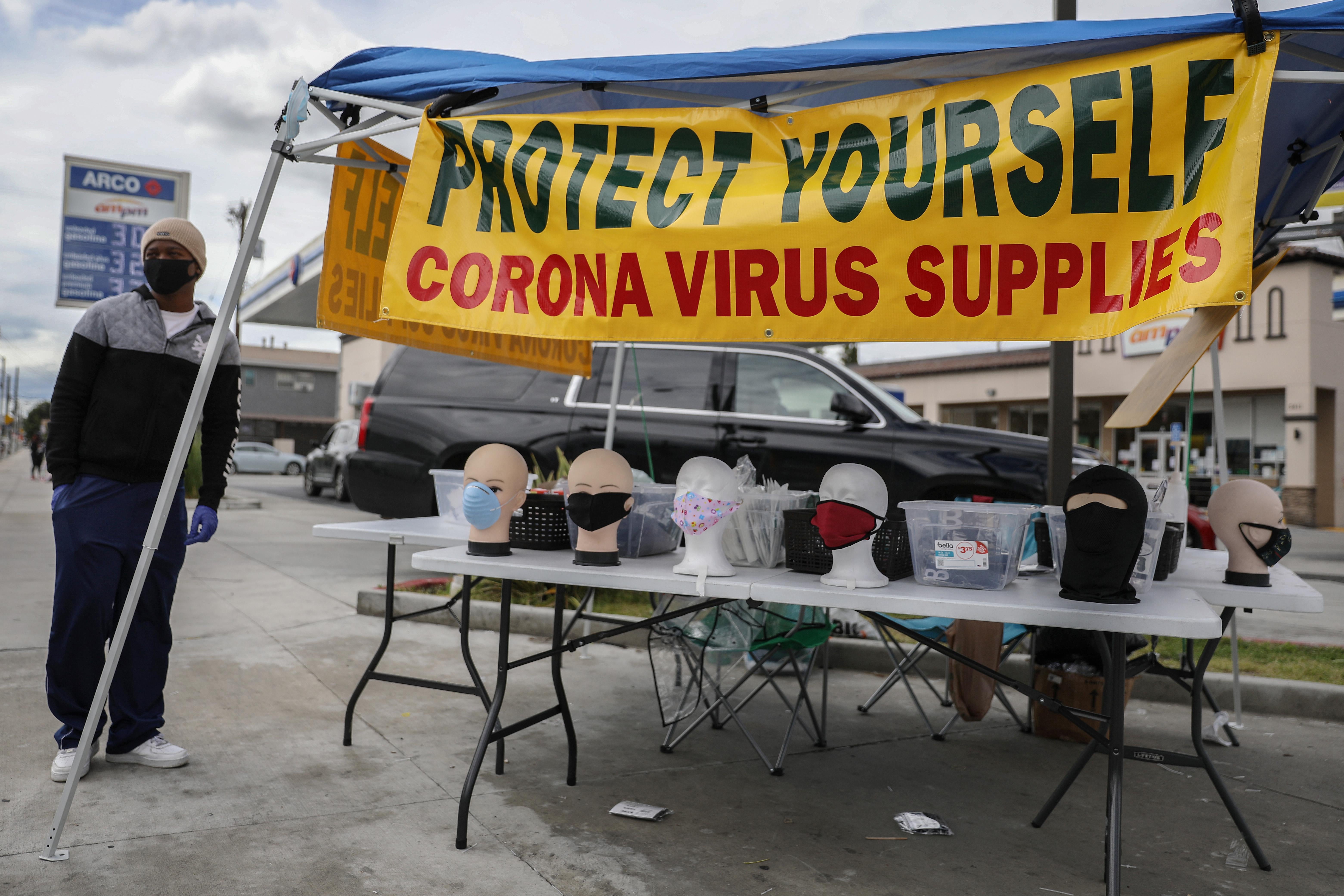 In a parking lot, a stand selling coronavirus supplies including face masks, with a sign that says "Protect Yourself"