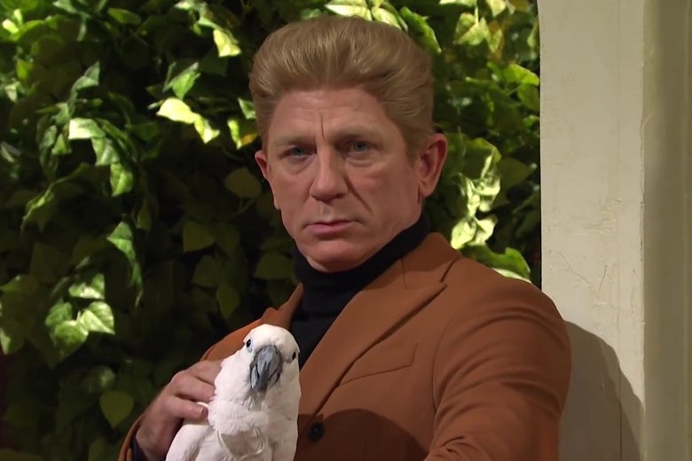 Daniel Craig in a blond pompadour wig, holding an exotic bird and making a dramatic expression.