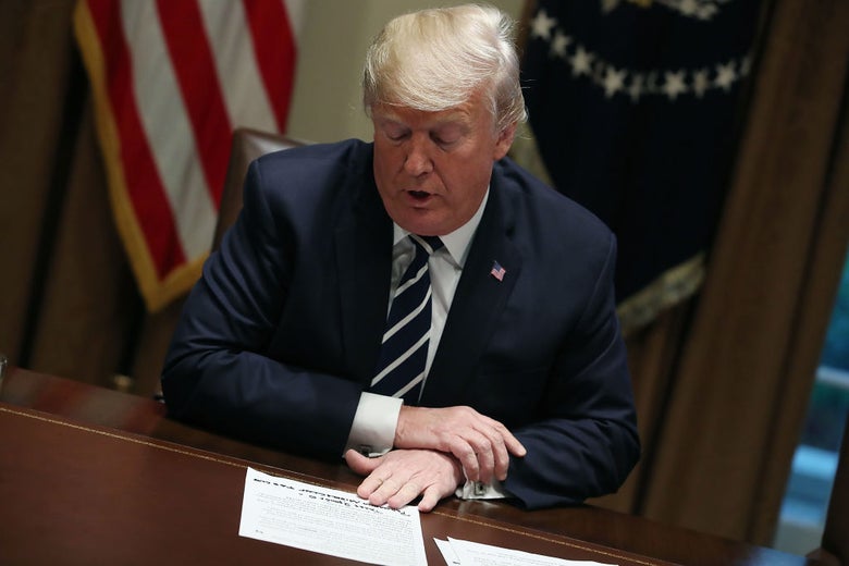 Trump, seated at a table, reads from notes on which written-in additions are visible.