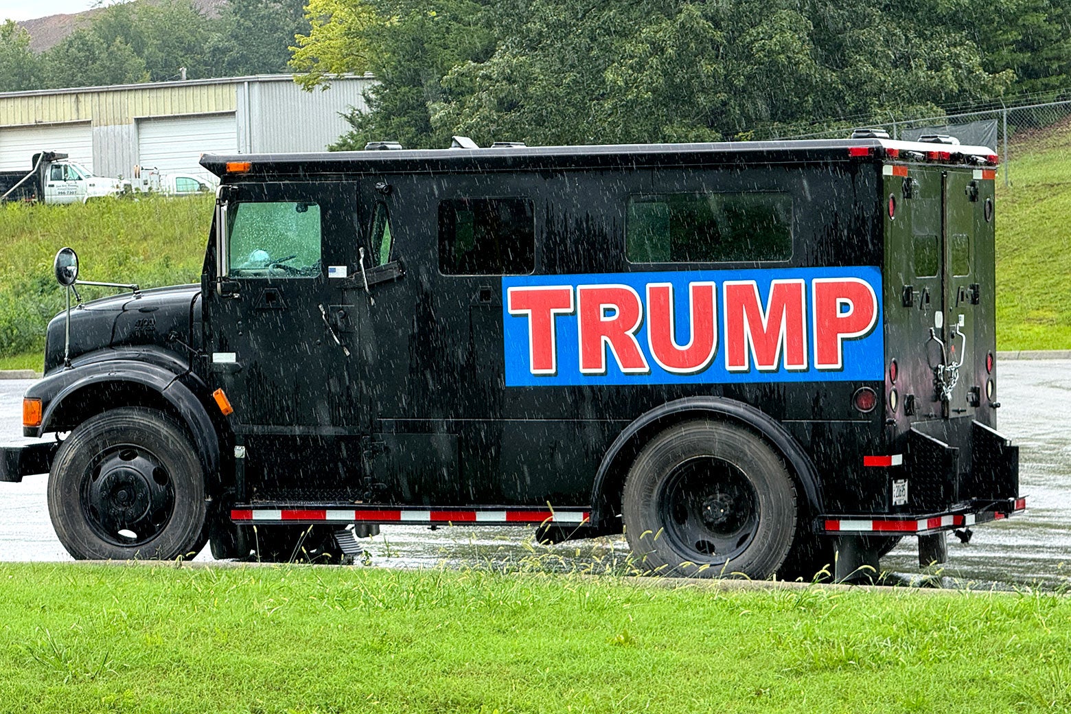 A heavy-duty black armored truck with a red Trump sign.