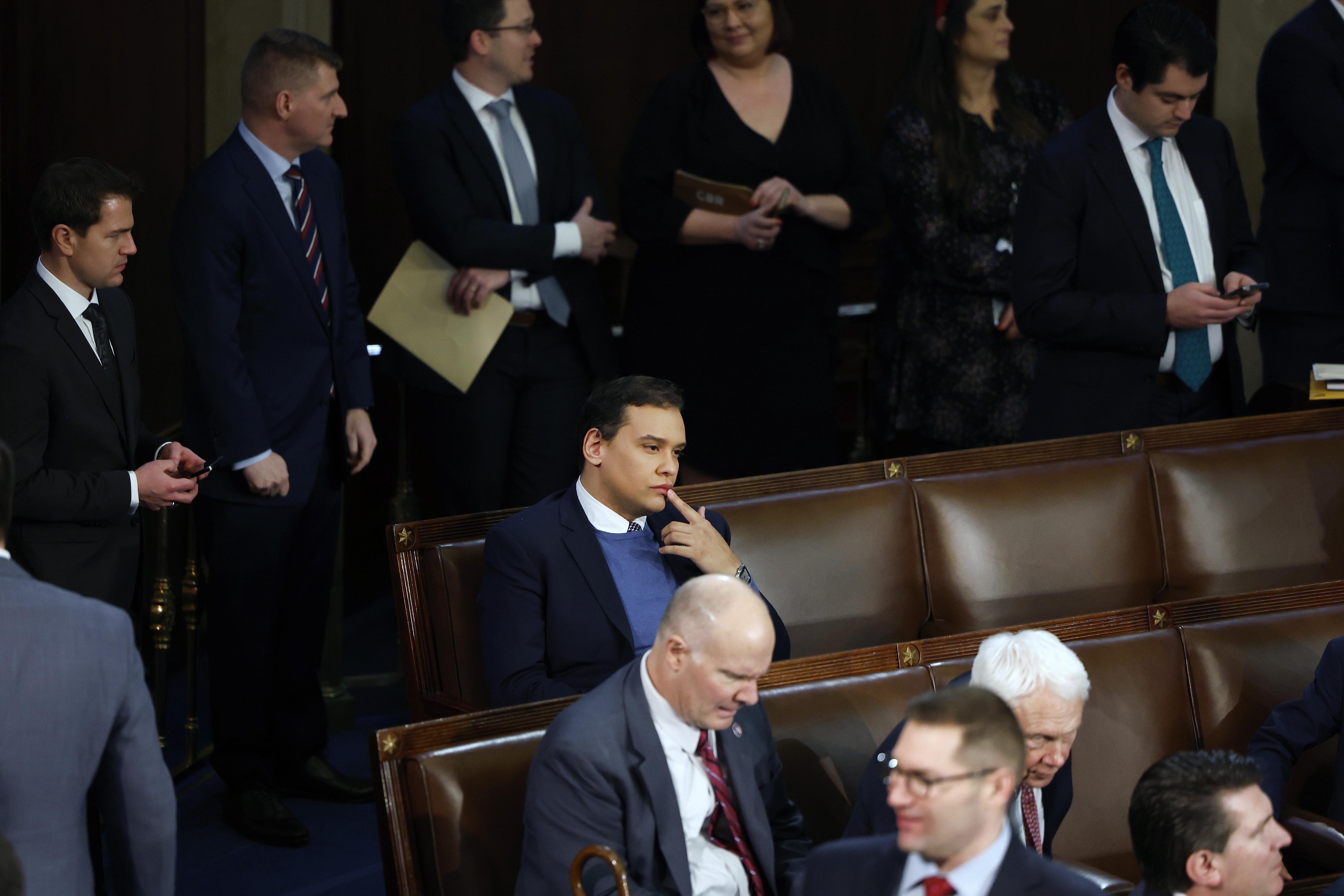 George Santos, an incoming House rep. from New York who lied about nearly every aspect of his background and biography, looking pensive, in the midst of other people shaking hands, in Congress.