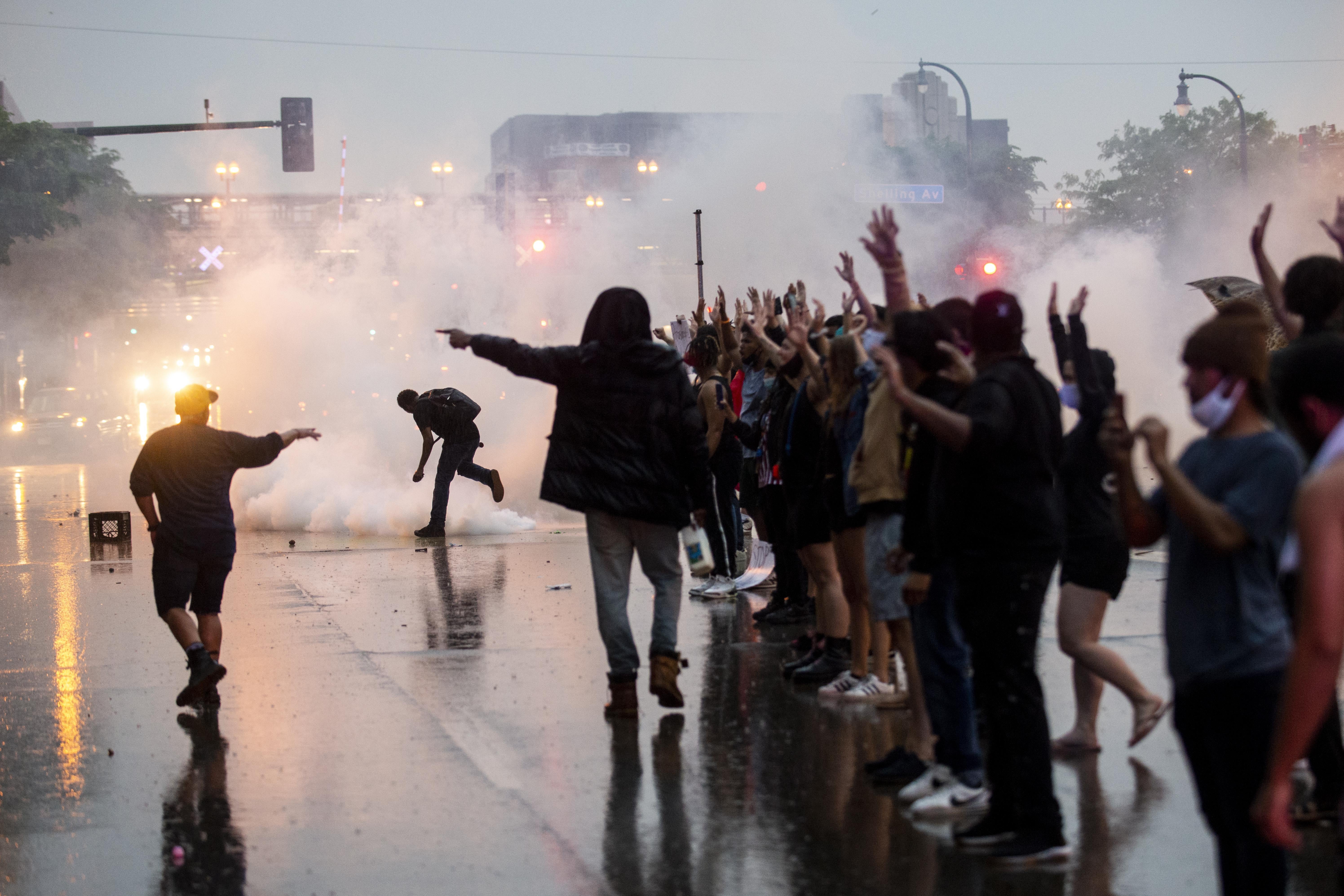 Protesters stand in a line in the street with their hands up as tear gas floods the scene.
