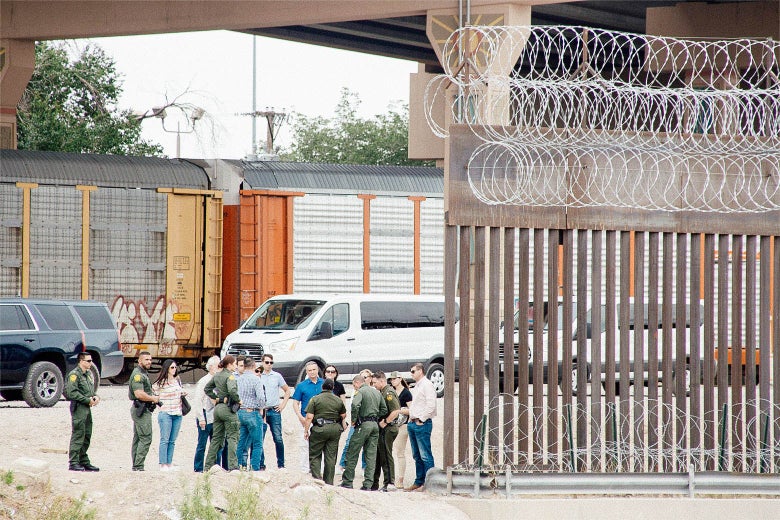 A crowd of people stand near the edge of the border wall.