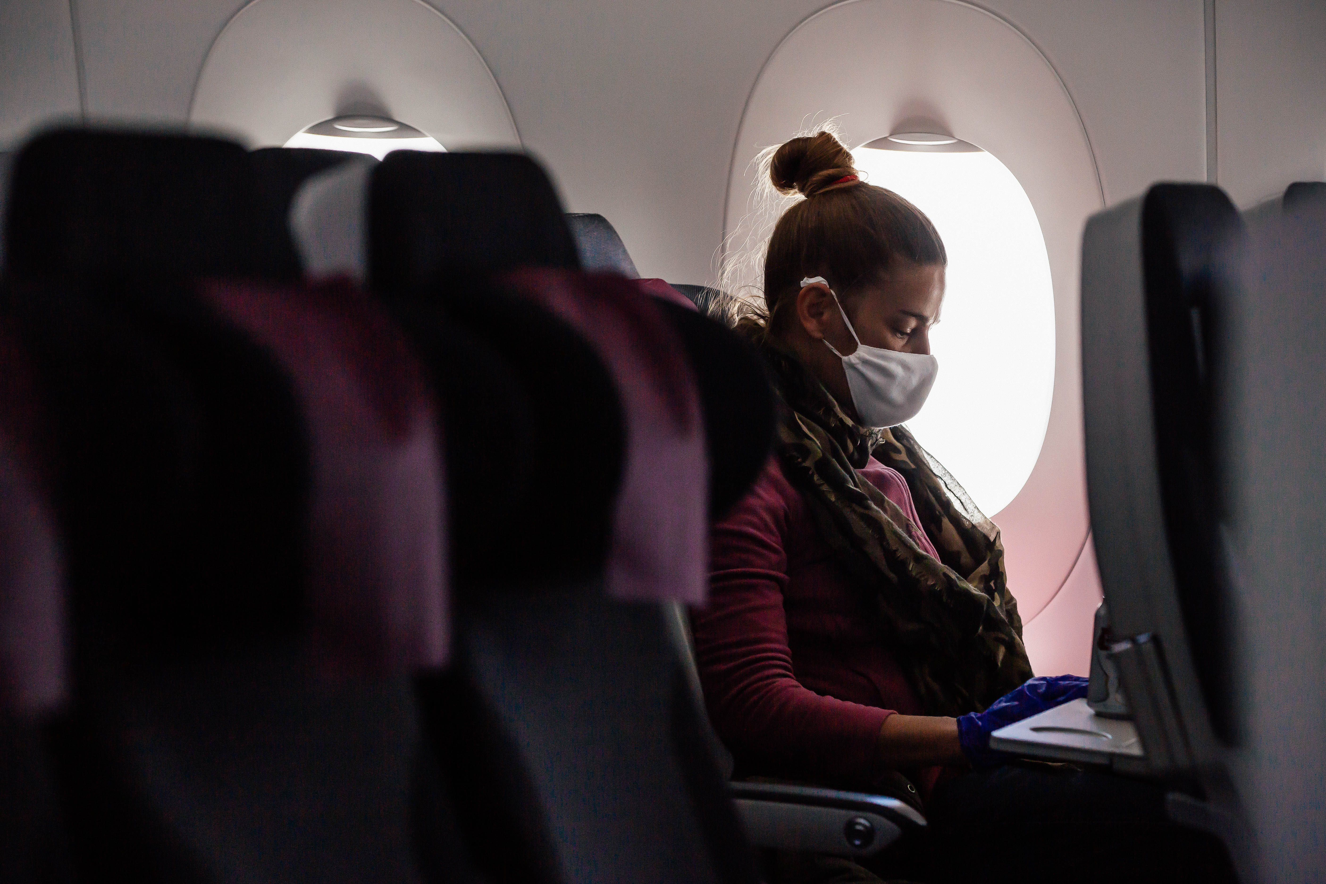 A woman wearing a mask sits on an airplane next to two empty seats.