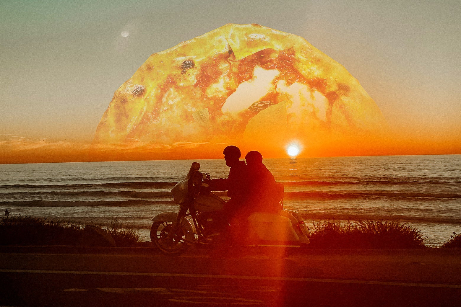 Two people ride a moped along the sea with a pizza sunset behind them.