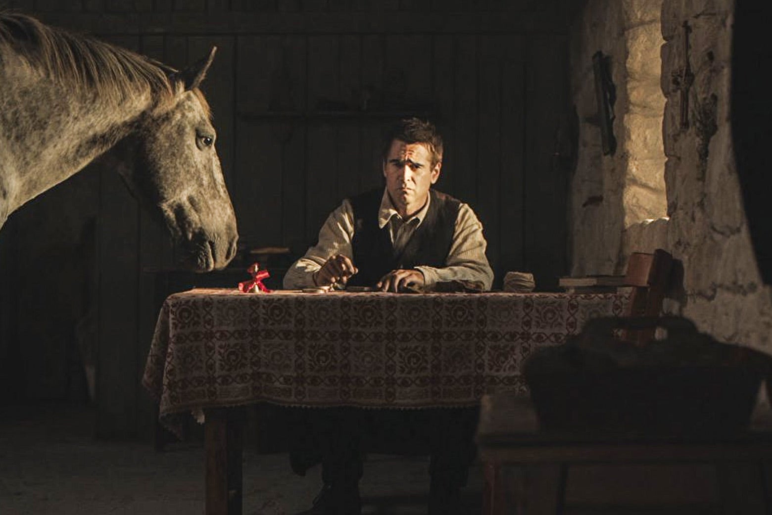 In a still from The Banshees of Inisherin, Colin Farrell sits in a rural home next to a donkey.