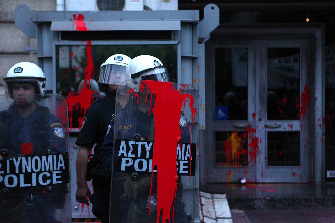 Riot police, hit by red paint ball stand guard as the protesters