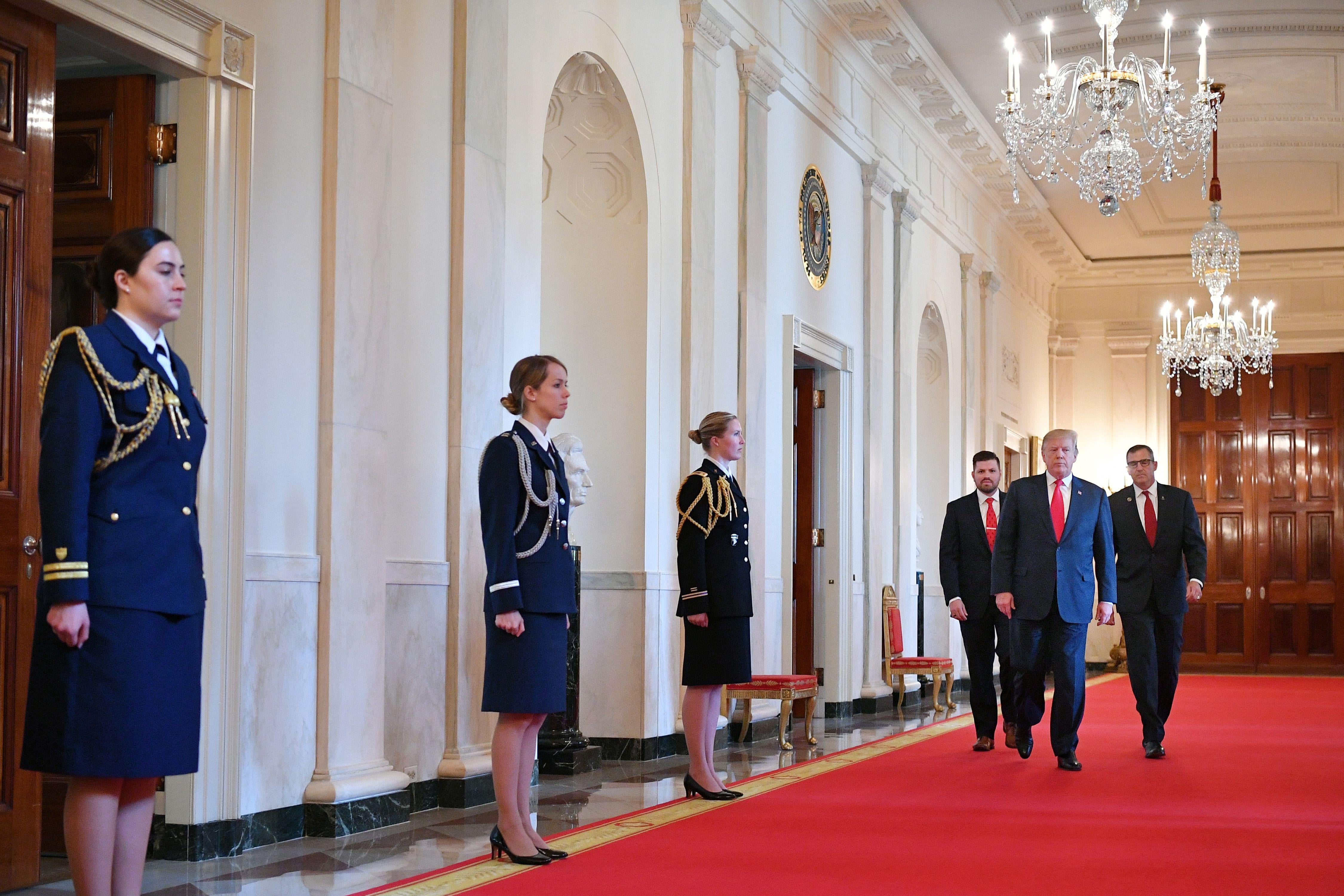 President Donald Trump walks through an ornate hall in the White House.