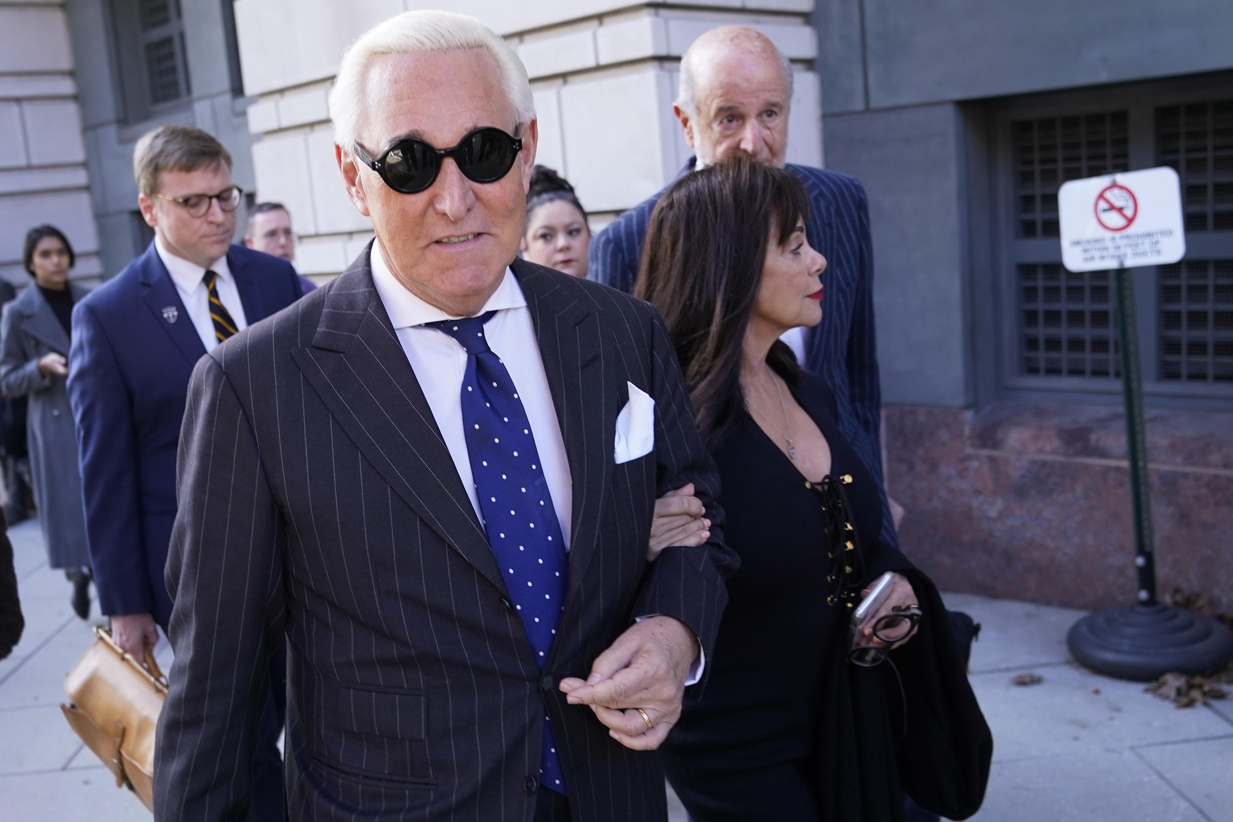 Roger Stone leaves a courthouse wearing some hip sunglasses and accompanied by his wife.
