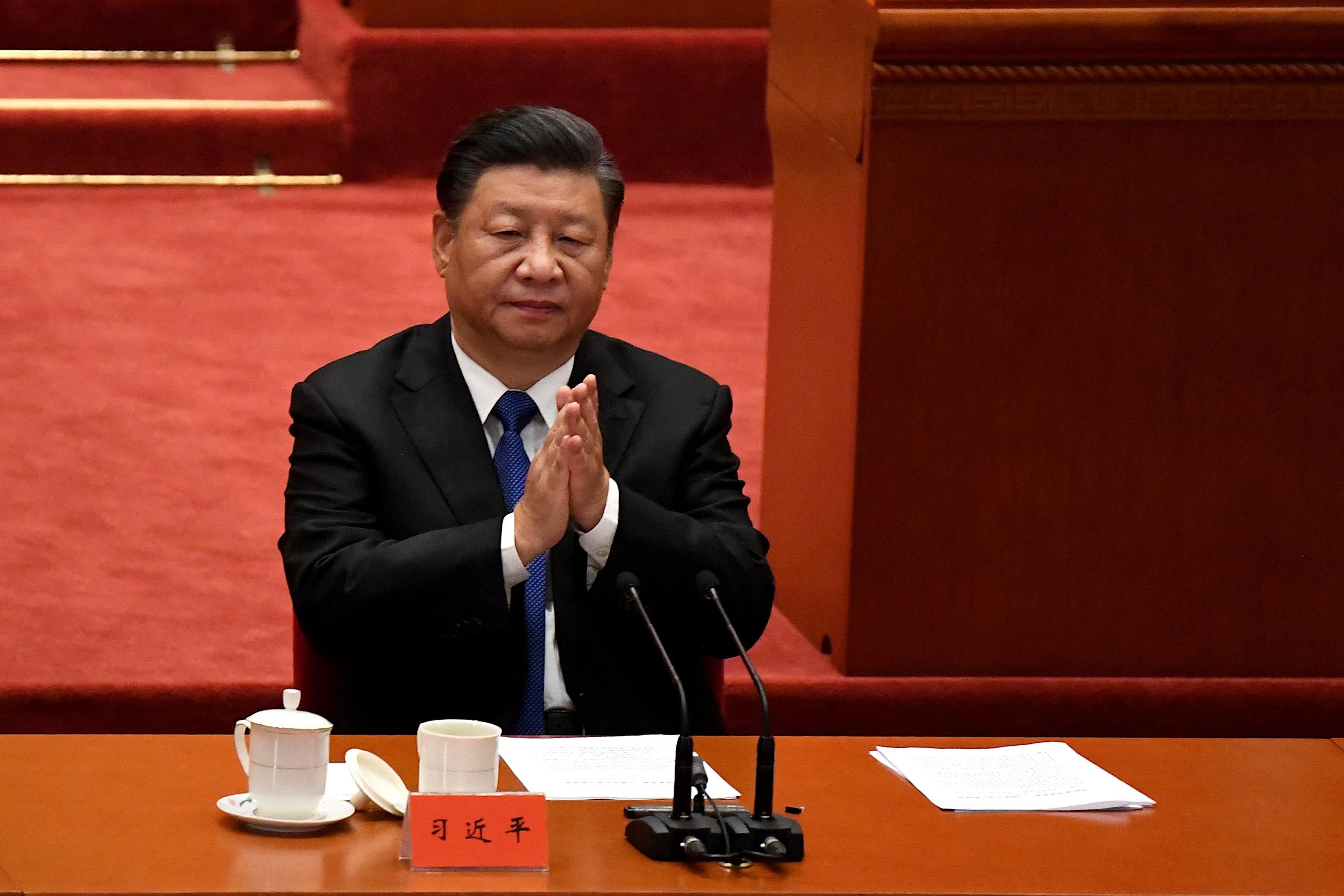 Xi Jinping sits at a table and folds his hands.