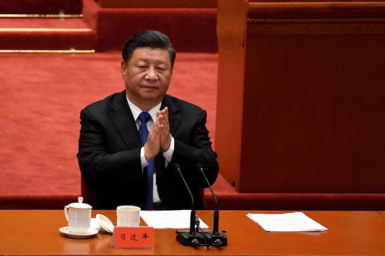Xi Jinping sits at a table and folds his hands.